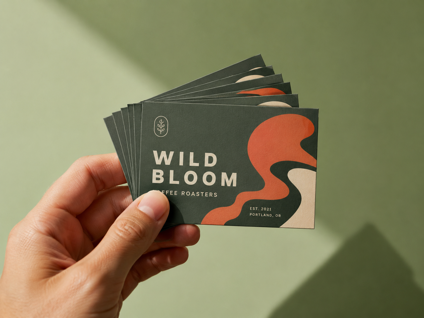 A hand fanning a stack of dark green business cards with a coral wave motif.