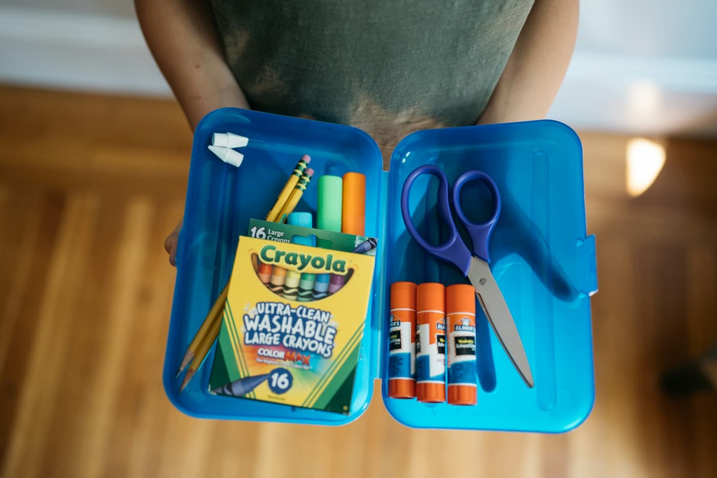 A blue pencil case of crayons, glue sticks and scissors.