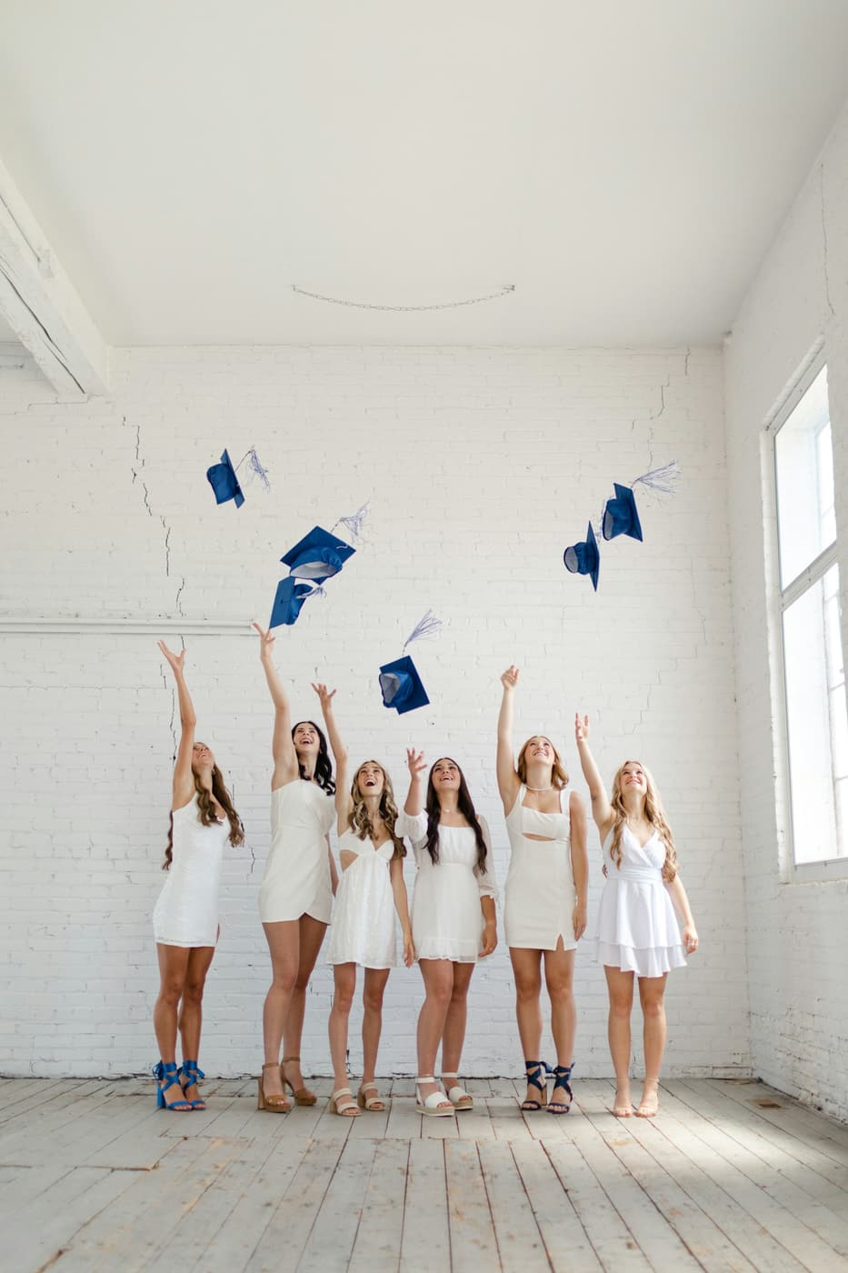 Graduates in white throwing their caps in the air.