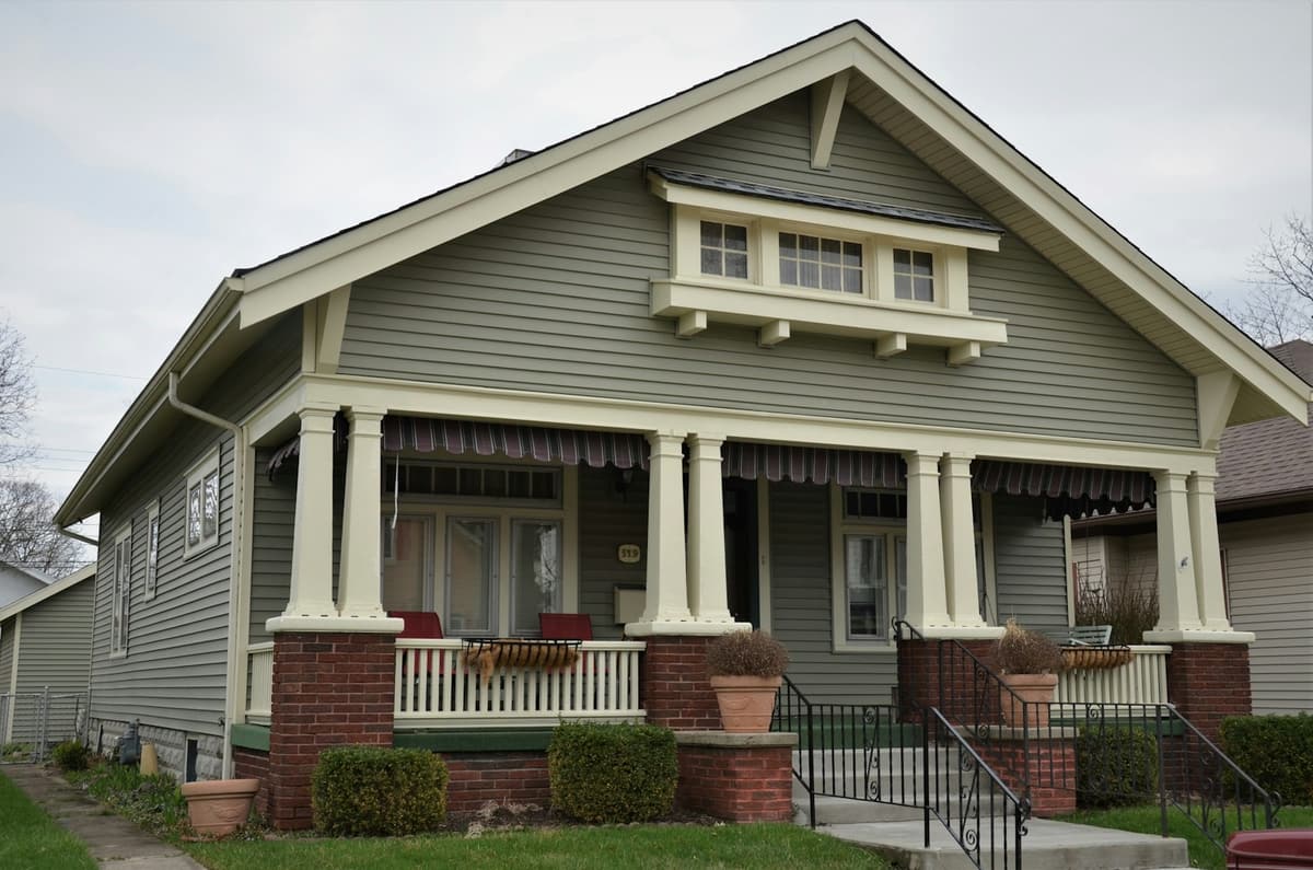 A craftsman house with a white porch and a front lawn.