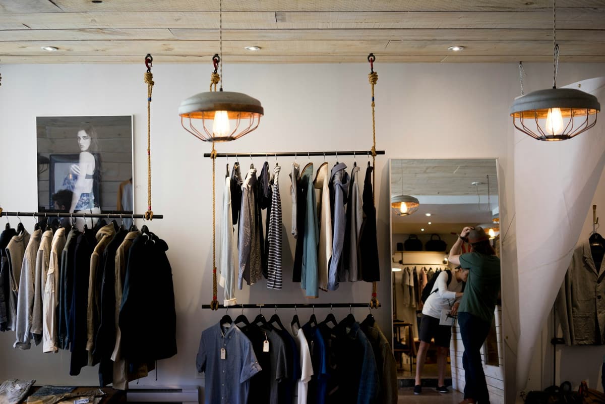 A boutique with clothing on hanging racks under pendant lights.